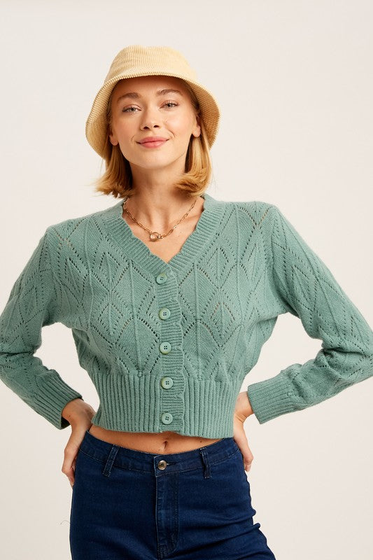 Knit Button Front Sweater with a cable knit design and cropped hem. Features a v-neck scallop edge neckline, front button-down closures, ribbed neck, cuffs, and hem for added texture and durability. Long sleeves and crochet knitting detail provide both warmth and elegance. Made from 52% acrylic, 25% nylon, 23% polyester. Free shipping on all orders. Shop now!