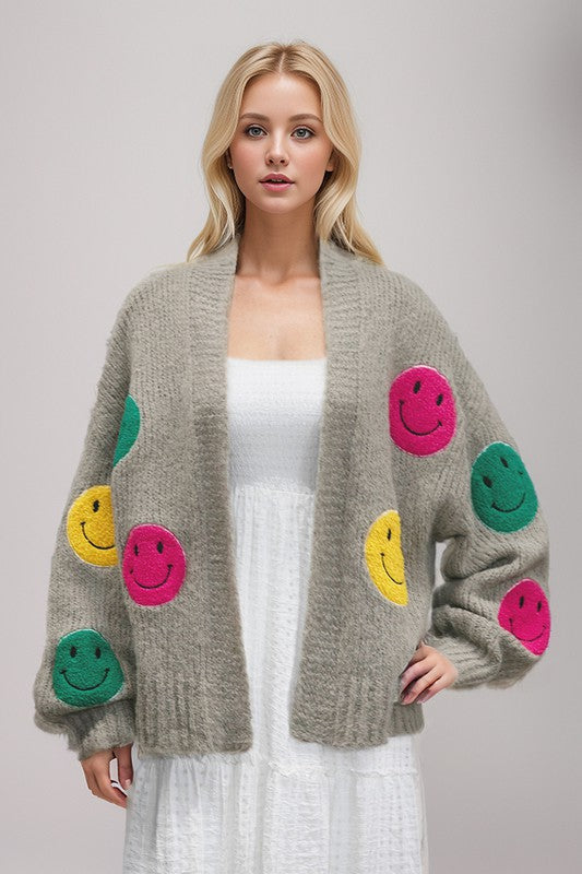 Fuzzy-Knit Cardigan with an oversized silhouette and a playful multi-color happy face at the front. Features ribbed cuffs, bell sleeves, and an open front for easy layering. A fun and stylish statement piece perfect for fashion-forward looks. Free shipping on all orders. Shop now!